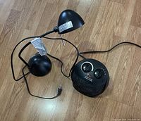 Photo of black electric space heater and small black desk lamp on wood floor with power cords visible