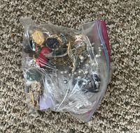 Clear plastic resealable bag containing assorted mixed costume jewelry including metal chains, beads, and other small pieces.