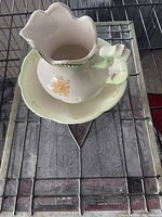Ceramic jug with floral pattern sitting inside a matching bowl, both light cream colored.