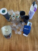 Photo showing the full lot including tumblers, shot glasses, water bottle cooler, can koozies, and digital kitchen scale on wooden surface.