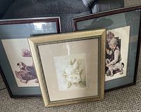 Three framed picture prints shown leaning against a sofa, including a floral print and two child and dog prints.