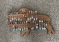 Photo of a wooden bull-shaped spoon holder displaying 36 souvenir collectible spoons with various designs and decorations.