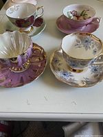 Four decorative teacups placed on matching saucers showing various floral and patterned designs, viewed from side angle.