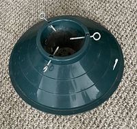 Side view of green plastic Christmas tree stand with three metal eyelet screws for securing tree.