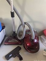 Shark red canister vacuum cleaner with hose and wand placed on table, showing vacuum base and hose connections