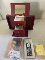Wooden jewelry box opened showing mirror, side compartments, drawers, and a set of colored markers and Oxford pencil tin beside it