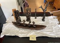Full view of five East African wooden carvings including a long canoe with four seated figures and four standing figures of varying abstract styles.