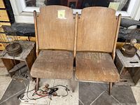 Front view of two connected antique wooden theatre seats with curved backs and worn finish showing delamination and surface wear.