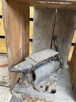 Photo of a heavy metal anvil placed on a wooden surface, showing rust and wear.