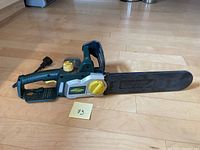 Full view of the electric chainsaw showing body, handle, chain cover, and power cord on wooden floor.