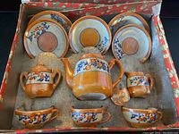 Photo of full tea set in original box showing teapot, creamer, sugar bowl, three cups, three saucers, two plates inside a red and green floral storage box.