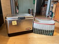 Photo showing both coolers side by side on floor, steel belted Coleman and soft Alite cooler.
