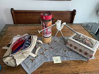 Photo of the lot on wooden table showing the Boye yarn swift, wicker sewing box, and fabric tote full of knitting needles.