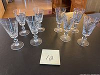 Eight cut crystal port/sherry glasses arranged in two rows on a black surface, showing two varying pinwheel cut designs.