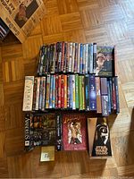 Overview of DVDs and VHS tapes placed on the floor including Harry Potter series, animated and live-action titles, and classic movie collections.