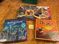 Photo showing three boxed board games including The Magic Labyrinth, Treasure of the Lost Pyramid, and Dixit on a wooden surface.