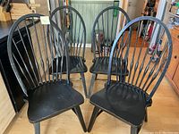 Four black wooden dining chairs arranged together indoors, showing overall shape and condition with worn paint visible.