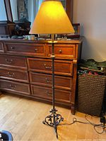 Full view of the floor lamp showing the yellow shade, metal pole, and power cord extending on floor.
