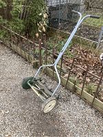 Side view of the manual push lawn mower showing the steel frame, wheels, and handle grips.