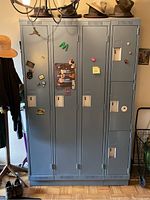 Front view of set of blue-gray metal lockers with three full height compartments and three smaller cubby compartments. Each locker door has magnets and stickers on it.