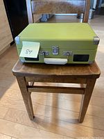 Closed green Crosley portable record player case on a wooden chair.