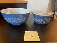 Photo showing both the medium-sized blue Pyrex bowl and the small casserole dish with clear glass lid, placed side by side on a black surface.