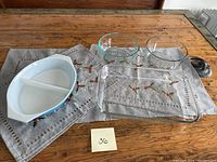 Full set of seven glass dishes including vintage divided Pyrex dish, two clear glass bowls, rectangular glass baking dish, two small Pyrex refrigerator dishes, and loaf-sized Glassbake dish on embroidered cloth