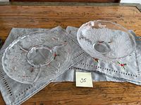 Both cut glass serving pieces displayed on a embroidered cloth. The divided platter shows clear sections with floral etching and scalloped edge, alongside the matching floral bowl.