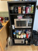 Black IKEA shelving unit holding kitchen items such as microwave, jars, mugs, toaster oven