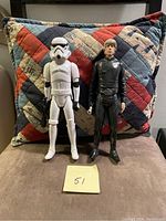 Both Stormtrooper and Luke Skywalker figures together in front of a quilted pillow.