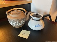 Photo of two tea pots on a table, showing the stoneware pot with bamboo handle and Corning Ware pot with blue floral design