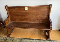 Front view of the antique wooden church pew showing the seat, backrest, and armrest ends.