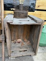 First photo showing an empty wooden beverage crate with slatted construction and cut-out side handles, some dirt and leaves inside.