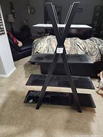 Full front view of black triangular shaped shelving unit showing four horizontal shelves and the unique frame shape with angled supports.