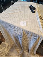 Full length view of one curtain panel draped over a table showing intricate lace pattern and tassels on one edge.