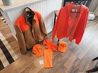 Full view of the lot showing two jackets and several orange hats laid on floor