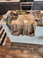 Camouflage jacket, pants, and tan utility vest laid out on counter