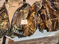 Two XL camouflage jackets laid out; one vinyl with light interior and Outdoor Life patch, the other a fleece-lined zip-up.