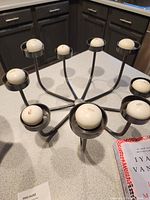 Metal candle holder set with nine round white candles placed on a kitchen counter with dark cabinets