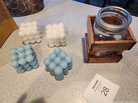 Four cube-shaped cluster candles in white and light blue colors, wood square holder with mason jar on a counter.