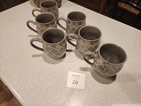 Six beige and cream ceramic coffee cups arranged on a countertop, showing the front and top view of the cups.