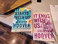 Photo of two paperback Colleen Hoover novels: "It Starts With Us" and "It Ends With Us" placed on a counter surface.