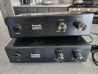 Two black Acoustic Audio WS1005 crossover subwoofers stacked on a countertop showing front panels with power, crossover, and sub volume controls.