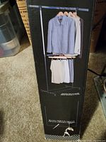 Box showing assembled garment rack with shirts and pants hanging on two tiers and wooden hangers.