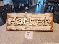 Front view of the wooden sign with raised metal letters spelling 'gather' on a distressed white background.