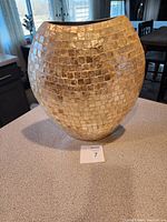 Front and side view of gold mosaic tile vase on kitchen countertop with furniture in background.