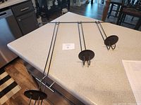 Top view of black metal hanging candle holder with three cylindrical candle holders, each with a circular base and hooks for hanging.