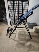 Side angled view of inversion table showing black metal frame and blue mesh backrest with headrest.