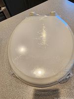 Toilet seat wrapped in protective plastic, showing white color and round front shape.