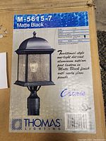 Box showing model M-5615-7 Matte Black outdoor post lantern by Thomas Lighting with product details.
